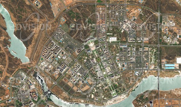 Das Satellitenbild "KANGBASHI - China" ist dem Bildband "CITIES - Brennpunkte der Menschheit" entnommen. Bildbeschreibung: ls im Jahr 2000 bei Dongsheng in der Inneren Mongolei, China, Kohle- und Gasvorkommen entdeckt wurden, setzte ein Aufschwung ein, der die Stadt rasch wachsen ließ. Um die erwartete Bevölkerungszunahme zu bewältigen, wurde  30 Kilometer von Dongsheng mit Kangbashi ein neuer Stadtteil erbaut. Auf 32 Quadratkilometern entstand zunächst für 300.000, später für fast 1 Million Menschen eine komplette Stadt. Diese wird allerdings von den Menschen nur zögerlich angenommen, wie die leeren Straßen im Satellitenbild zeigen. Bis 2015 waren erst etwa 100.000 Menschen in diese „Geisterstadt“ gezogen.