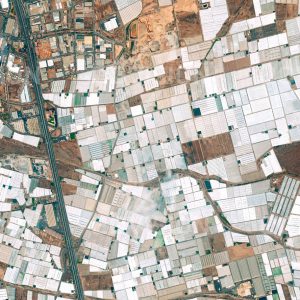 Das Satellitenbild "EL EJIDO - Spanien" ist dem Bildband "HUMAN FOOTPRINT - Satellitenbilder dokumentieren menschliches Handeln" entnommen. Bildbeschreibung: Unterirdische Wasservorräte und das Was­ser aus den Ausläufern der Sierra Nevada ermöglichen in der unfruchtbaren Wüste um El Ejido in Südspanien die Bewirtschaftung der weltweit größten Anbaufläche unter Folie. Zu der durch Wasserverbrauch und Pestizideinsatz im mehr als 360 Quadratkilometer umfassenden „mar del plástico“ (Plastikmeer) bedenklichen ökologischen Situation gesellen sich soziale Probleme schlecht bezahlter Arbeitskräfte.