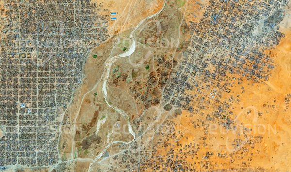 Das Satellitenbild "AL FĀSHIR - Sudan" ist dem Bildband "HUMAN FOOTPRINT - Satellitenbilder dokumentieren menschliches Handeln" entnommen. Bildbeschreibung: Als Folge des Darfur-Konflikts, der ab 2003 den Sudan erschütterte und annähernd 300.000 Todesopfer forderte, verloren etwa fünf Millionen Menschen ihre Heimat und fanden in Flüchtlingslagern Zuflucht. So entstand auch im Norden der Stadt al-Fashir im Winter 2004/05 der erste Teil des Flücht­lingslagers Abu Shouk, eine Erweiterung nach Osten folgte in den Jahren danach. Der regelmäßige Aufbau des innerhalb weniger Jahre entstandenen Lagers unterscheidet sich deutlich von der gewachsenen Struktur der ursprünglichen Siedlung.