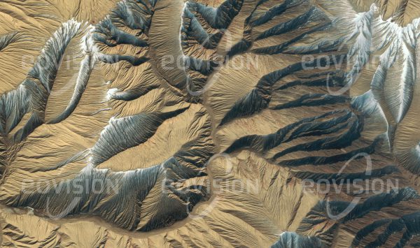 Das Satellitenbild "KUNLUN SHAN - China" ist dem Bildband "UNTOUCHED NATURE - Naturlandschaften in Satellitenbildern" entnommen. Bildbeschreibung: Im Übergang zum Tarim-Becken erreichen die Ausläufer des Kunlun Shan noch Höhen bis 3.000 Meter. Fern von den Ozeanen und ringsum von hohen Gebirgszügen umgeben, gehört das Tarim-Becken zu den trockensten Gebieten der Erde. Der Lichteinfall und der in den Schattenhängen liegen gebliebene Schnee lassen hier das fein verästelte Ero­sionsmuster in den fast vegetationslosen, weichen Schichten des Sedimentgesteins deutlich hervortreten.