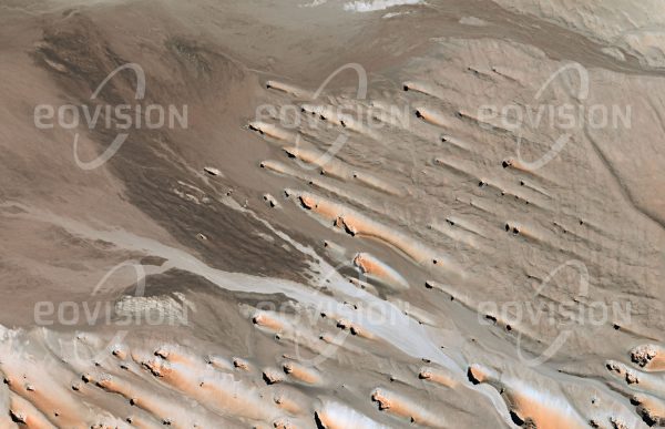 Das Satellitenbild "PAMPA DE LOS BAYOS - Argentinien" ist dem Bildband "WÜSTEN - Lebensraum der Extreme" entnommen. Bildbeschreibung: Die Anden im Nordwesten Argentiniens sind stark von Vulkanismus geprägt. Dies trifft auch auf die Sierra Aguas Dulces zu, an die sich diese Hochebene anschließt. Hier wirken Wind und Wasser in entgegengesetzter Richtung. Während die seltenen Niederschläge am flachen Hang nach Westen abfließen, lagert der Wind den Sand im Windschatten östlich der Felsen ab.