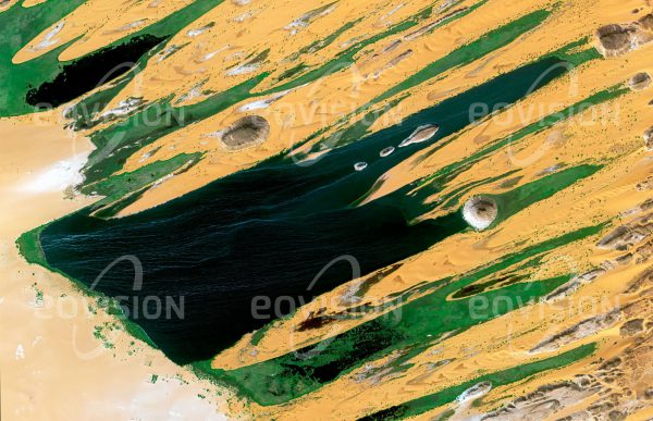 Das Satellitenbild "LAC TELI - Tschad" ist dem Bildband "WÜSTEN - Lebensraum der Extreme" entnommen. Bildbeschreibung: Zwischen den Gebirgen des Tibesti und des Ennedi liegen die Ounianga-Seen, die größten Seen der Sahara. Sie sind Reste eines einst deutlich größeren Sees, der auch den heutigen Tschadsee einschloss. Der Salzsee Lac Teli ist der größte See der Ounianga-Serir-Gruppe, der zweitgrößten Gruppe der Ounianga-Seen. Spezielle hydrogeologische Verhältnisse verhindern, dass trotz der starken Verdunstung von mehr als 6000 Millimetern Wasser pro Jahr die anderen Seen versalzen. Die Größe und Form der Seen wird von Wanderdünen beeinflusst, die von den vorherrschenden Nordostwinden verlagert werden. Spuren des Menschen reichen bis weit in vorgeschichtliche Zeiten zurück, als die Sahara noch keine Wüste war.